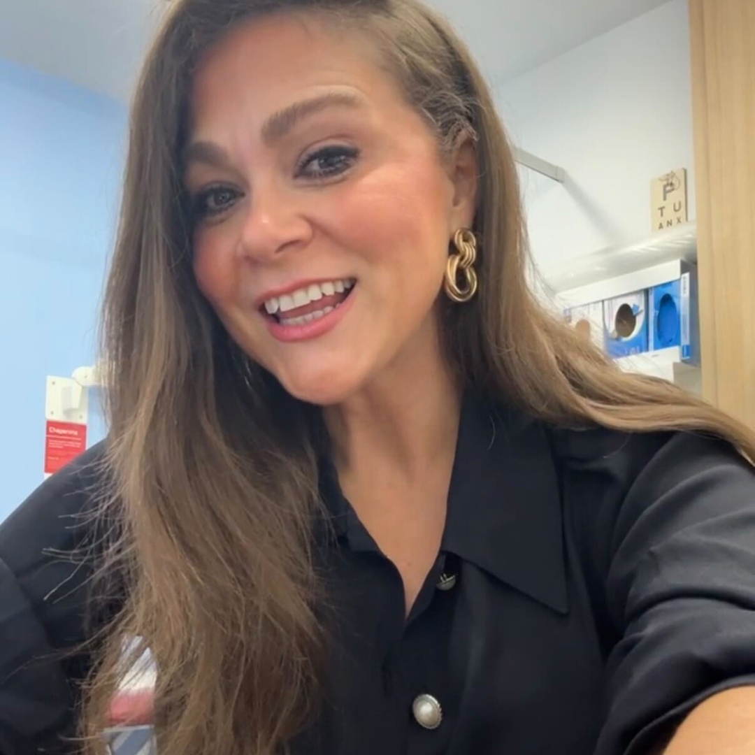Smiling woman in a black collared blouse wearing large gold intertwined hoop earrings, head-and-shoulders close-up.