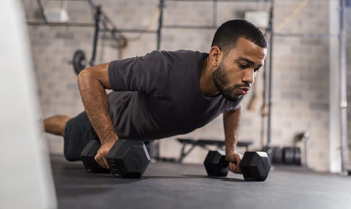 Man doing push-up gripping two black hex dumbbells, low-angle close-up on his upper body and focused expression.