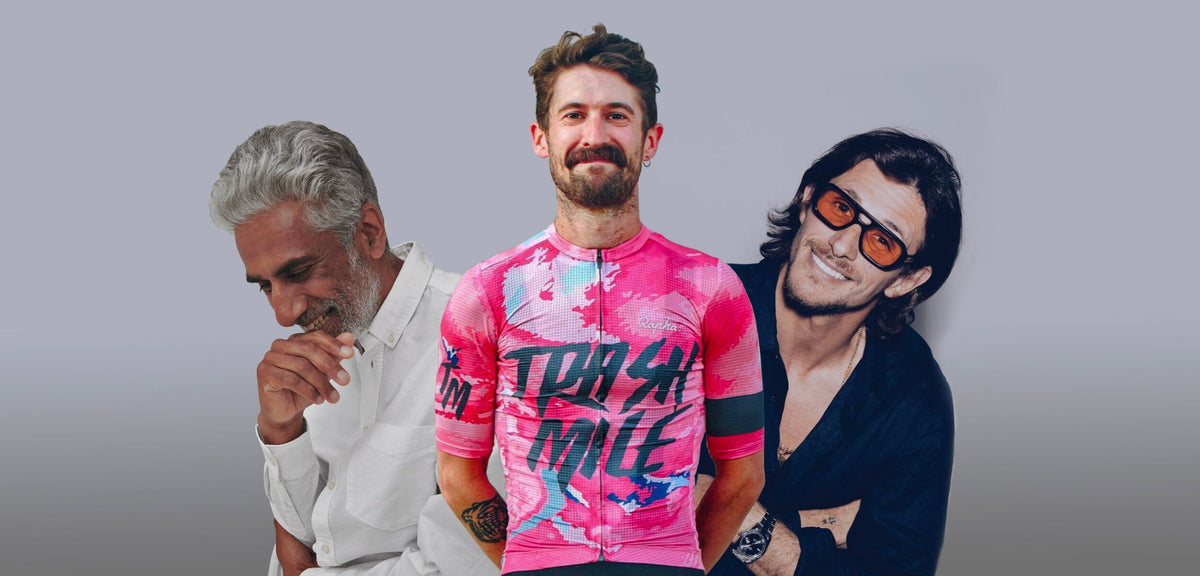 Three men waist-up on gray backdrop; center man wears bright pink cycling jersey reading TRASH MILF, others smile.