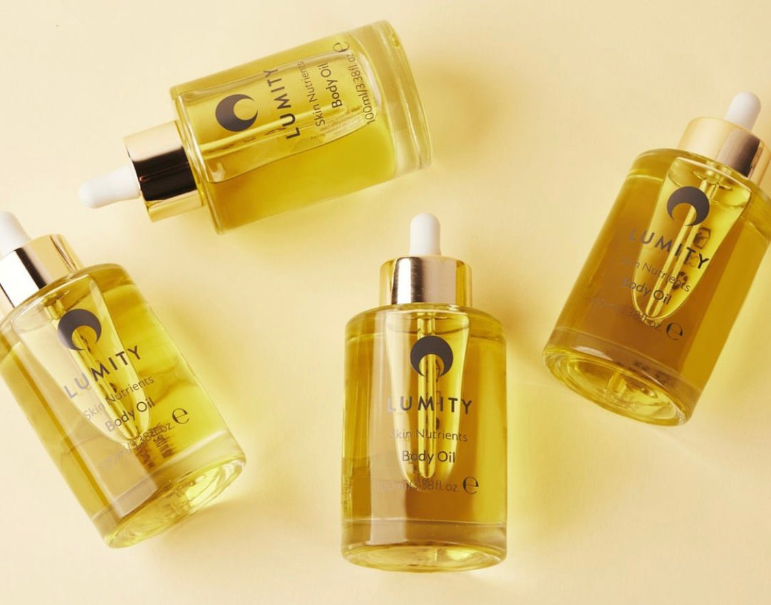 Lumity body oil in clear glass with gold collars and white droppers, four bottles, two upright, one tilted, one on side