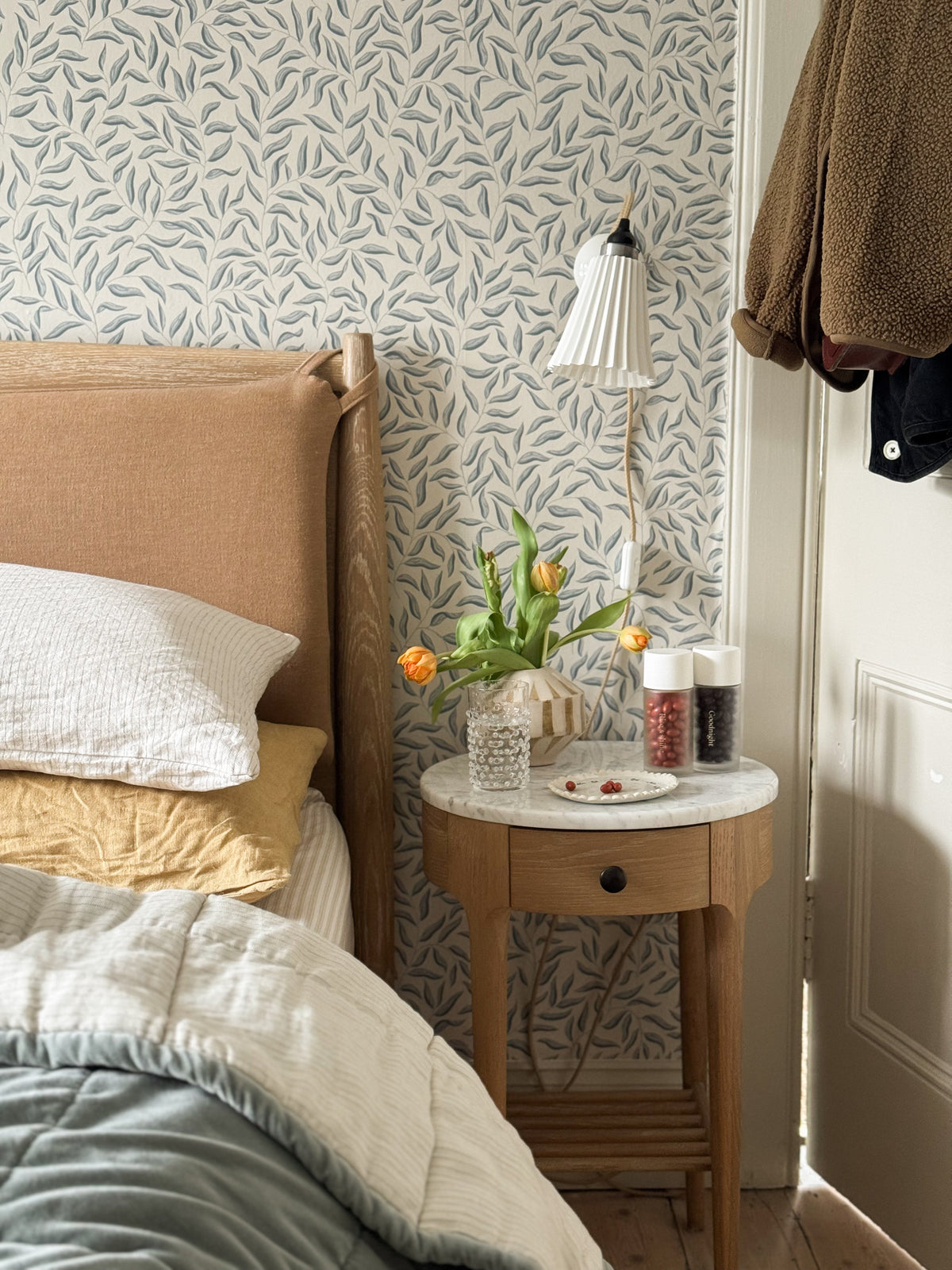 Cozy bedside with white quilted pillow, mustard-yellow cushion, wooden nightstand with orange tulips, water glass, red berries