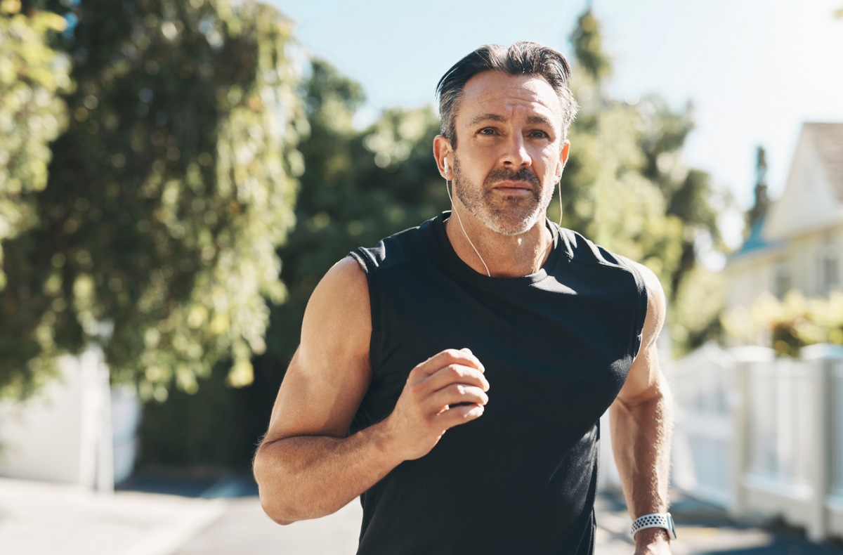 Close-up of a middle-aged man jogging, short dark hair with gray, wearing a black sleeveless shirt, earphones and a smartwatch.