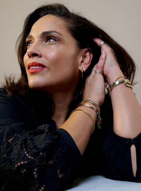 Woman in black lace top with red lipstick, looking upward, chin resting on hands showing gold bracelets and hoop earrings.