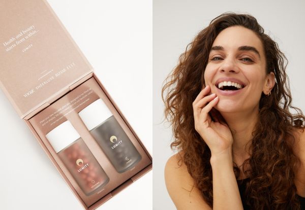 Two Lumity translucent matte bottles with white caps in a pale pink box beside a smiling woman touching her cheek