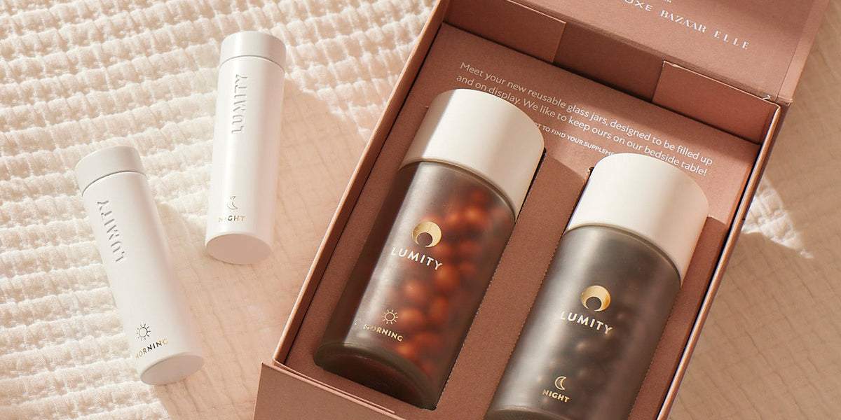 Lumity Morning & Night: frosted glass jars with white caps and capsules in an open box, two white tubes on light fabric