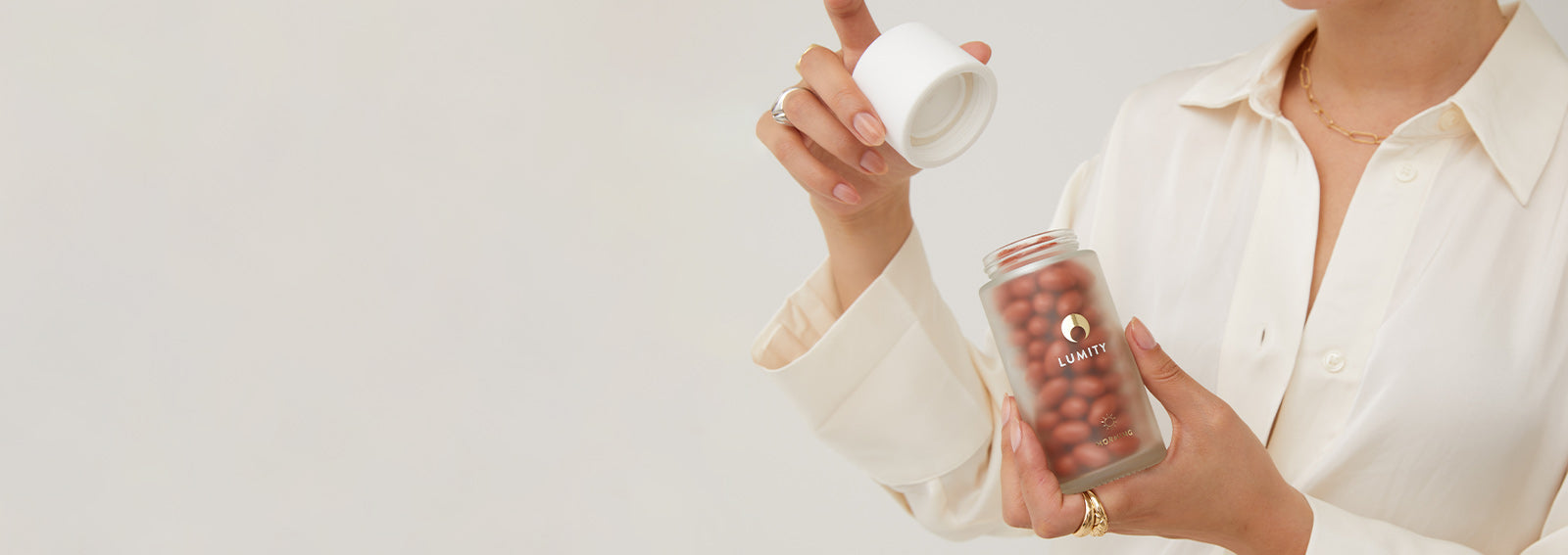 Hand opening a frosted glass bottle with Lumity female supplements in it