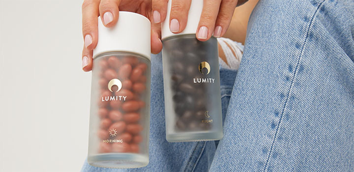 Woman wearing jean trousers holding Lumity frosted glass bottles filled with softgels