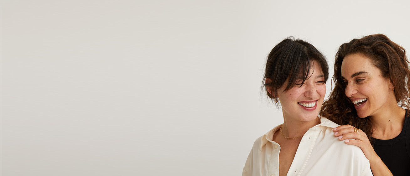 Two women smiling - woman behind has her hand on the shoulders of the woman infront