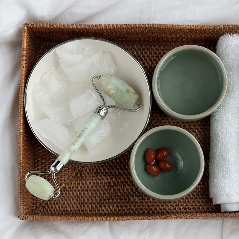 Tray with a bowl of ice, Lumity Jade Facial roller, small bowls with 4 Lumity Morning Softgels, and a towel on a white background.