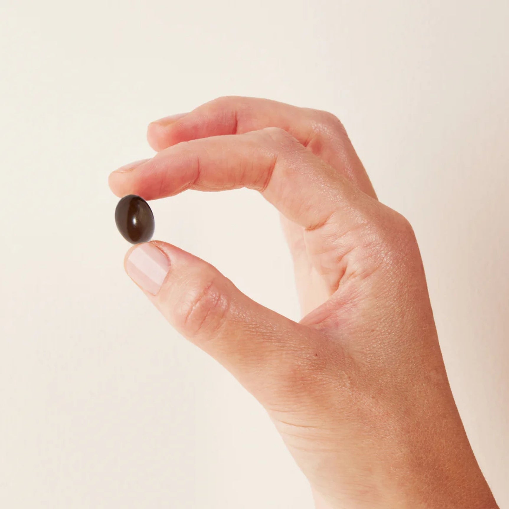 Hand holding a dark softgel from a Morning & Night Women's Supplement for daily wellness support