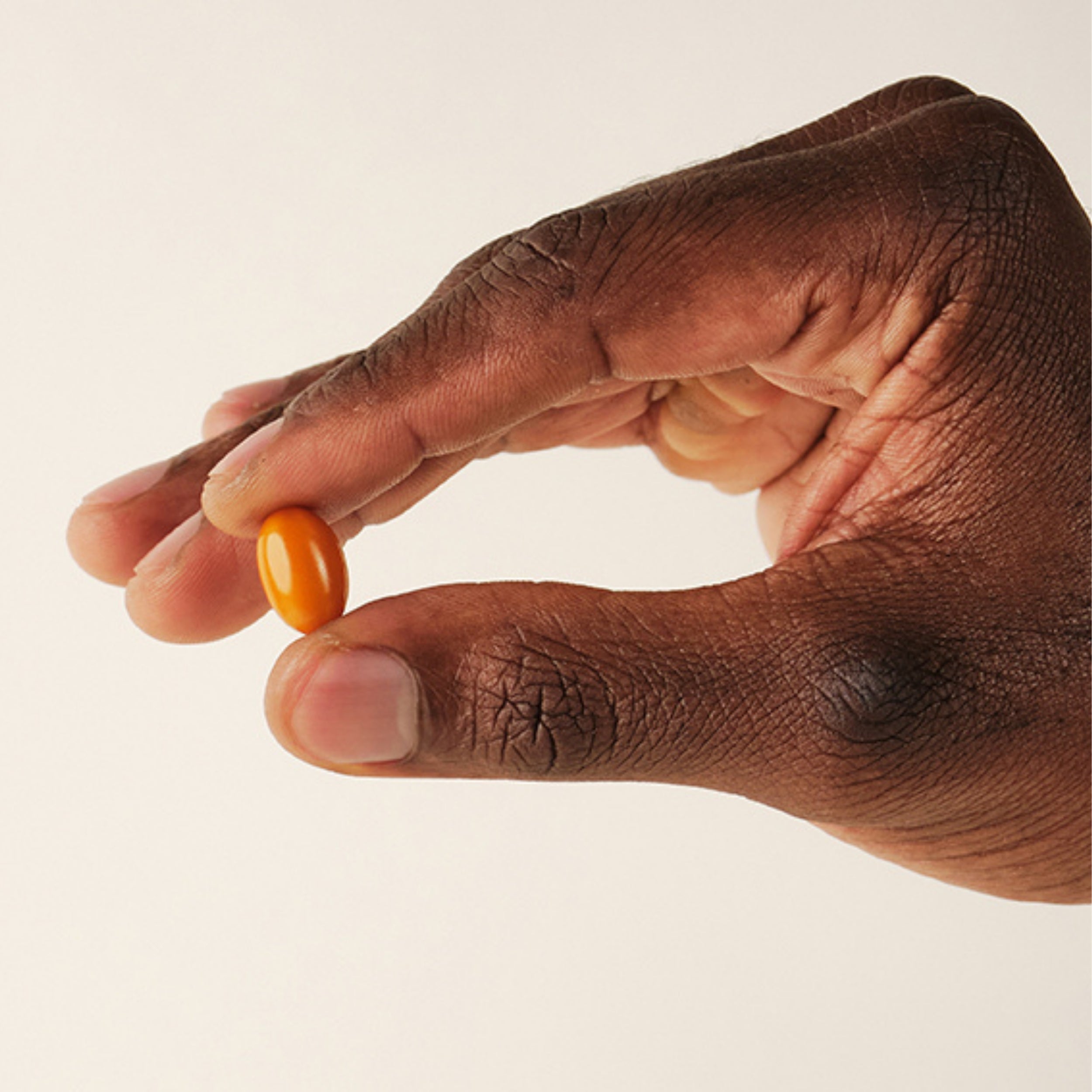 Hand holding an orange softgel from a morning and night male supplement daily routine for vitality support