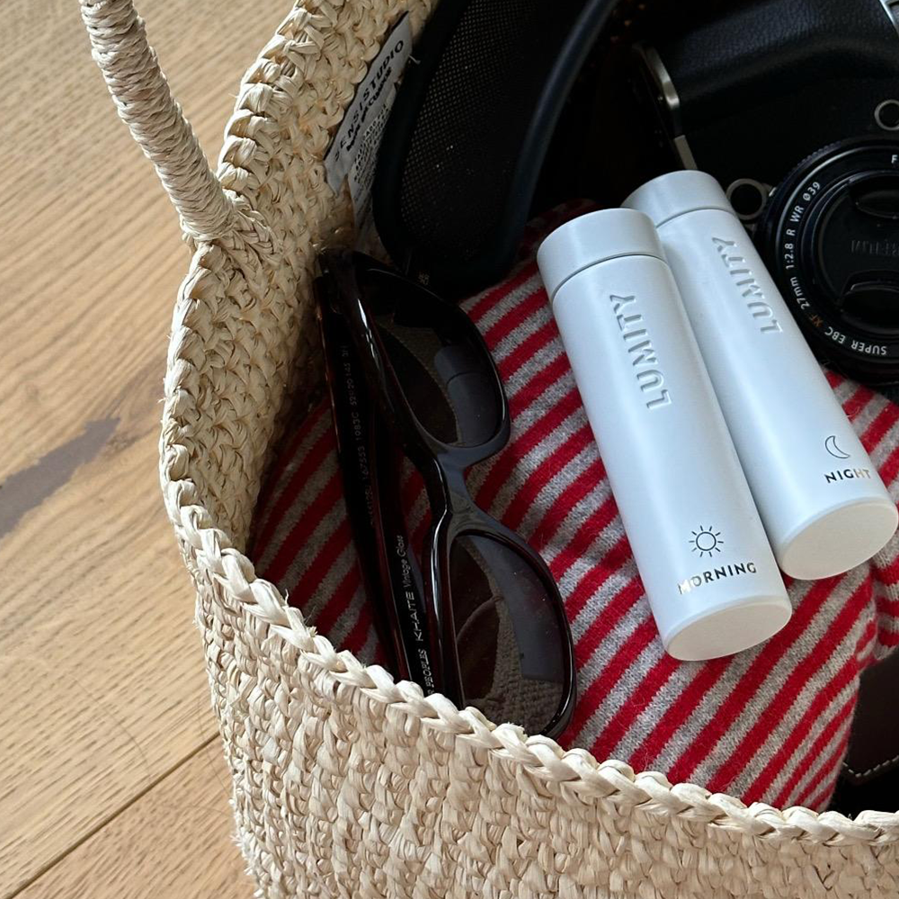 Woven bag with sunglasses and Lumity Morning & Night Supplement Travel Cases, a camera and a towel inside