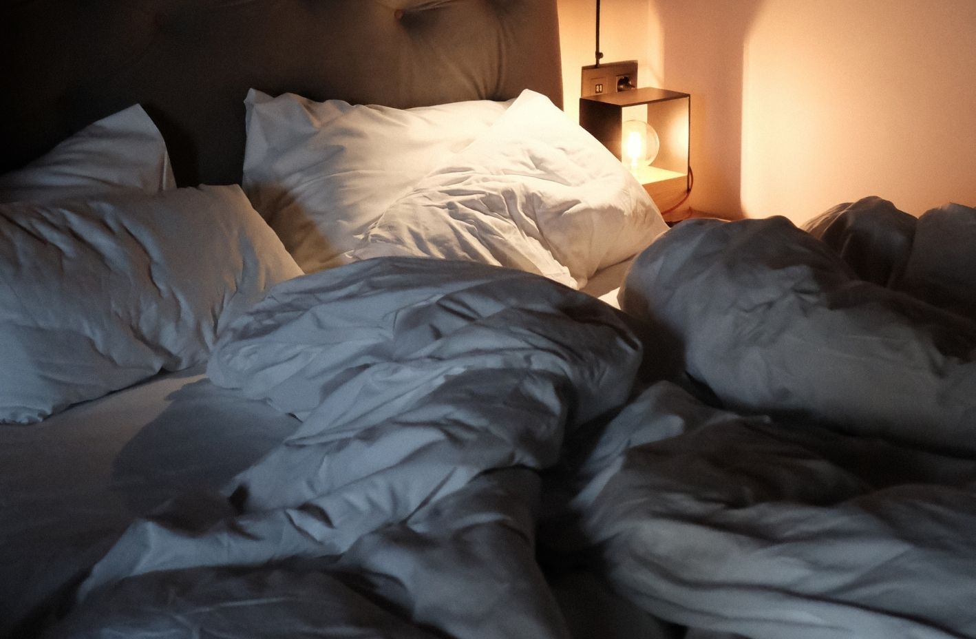 Photo of unmade bed with bedside lamp.