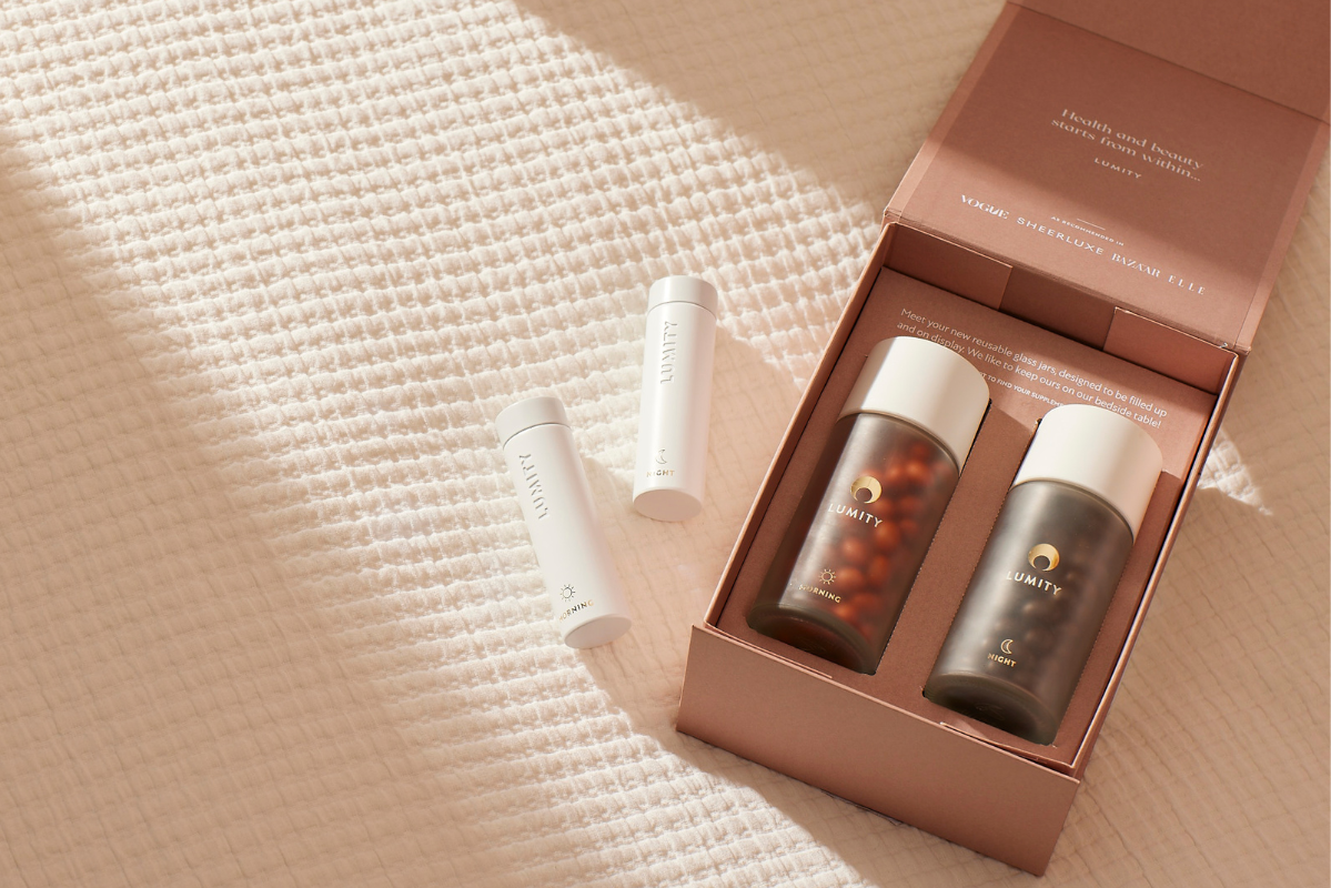 Lumity morning (orange capsules) and night (dark capsules) glass jars in pink box with two white bottles, slight top-down view
