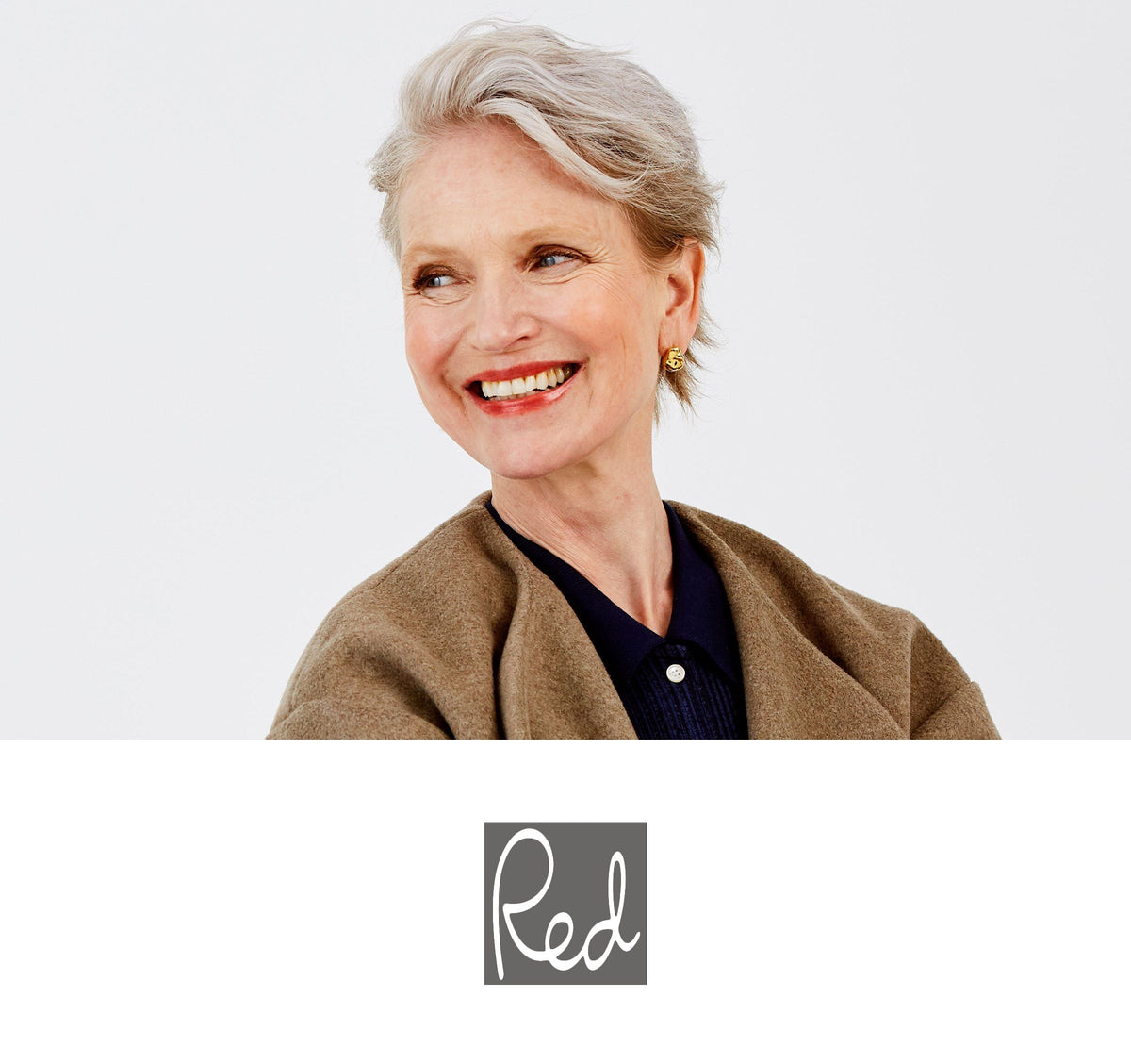 Smiling older woman with short gray hair and gold earrings in a brown coat; white background with a gray box reading 'Red'.