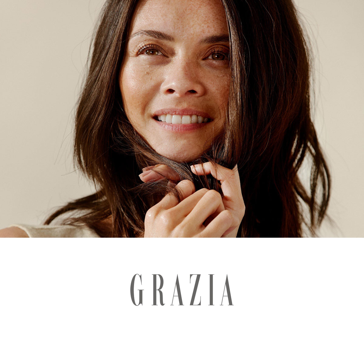 Close-up of a smiling woman with medium skin tone, freckles and long dark brown hair held near her mouth; 'GRAZIA' below.