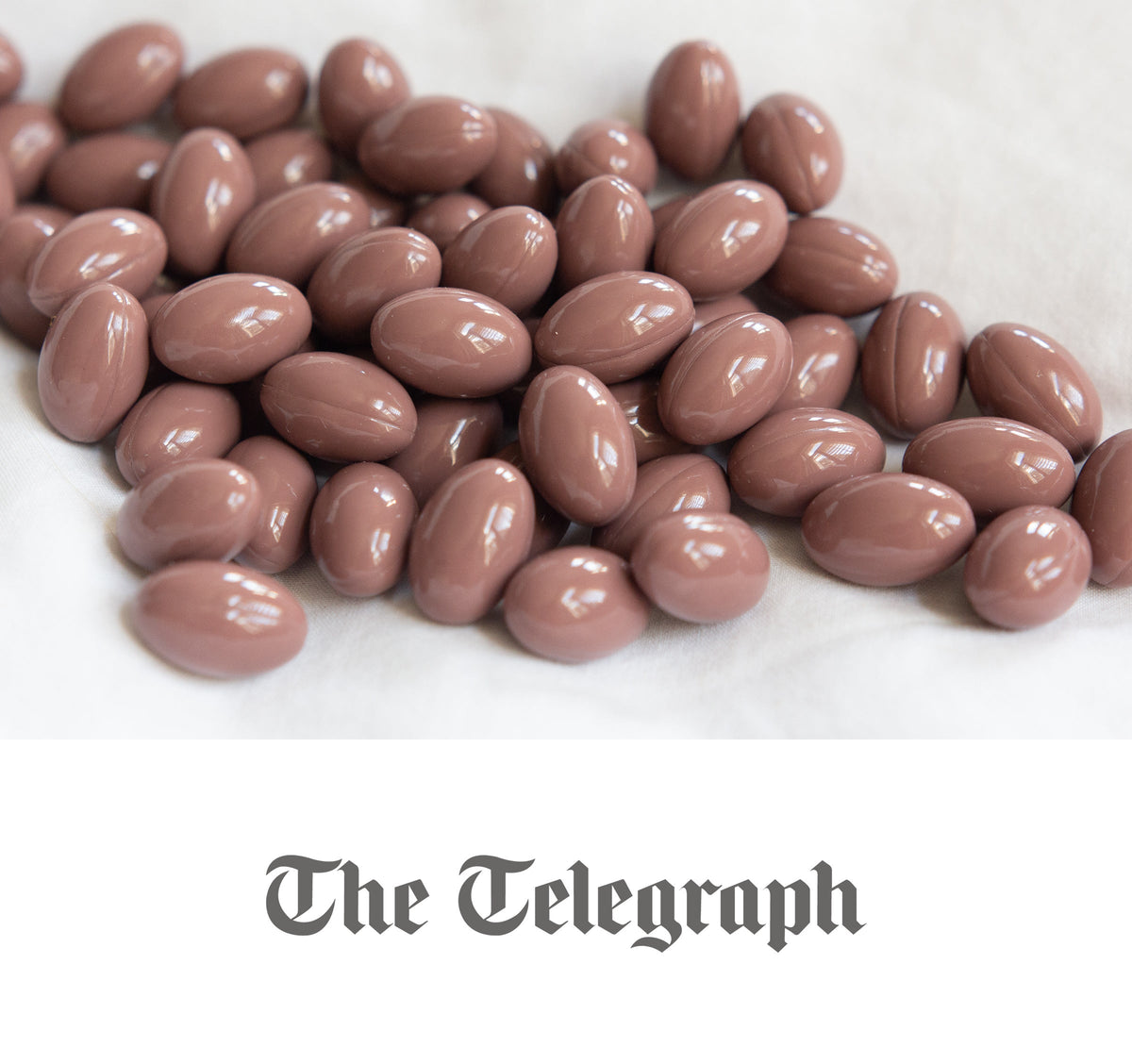 Brown glossy oval capsules scattered on a white cloth, overhead slightly angled close-up with shallow depth of field