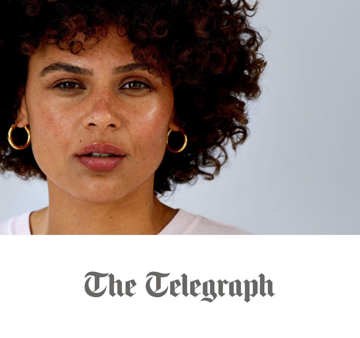 Close-up portrait of a woman with medium brown skin, curly dark hair, gold hoop earrings and a light pink top.