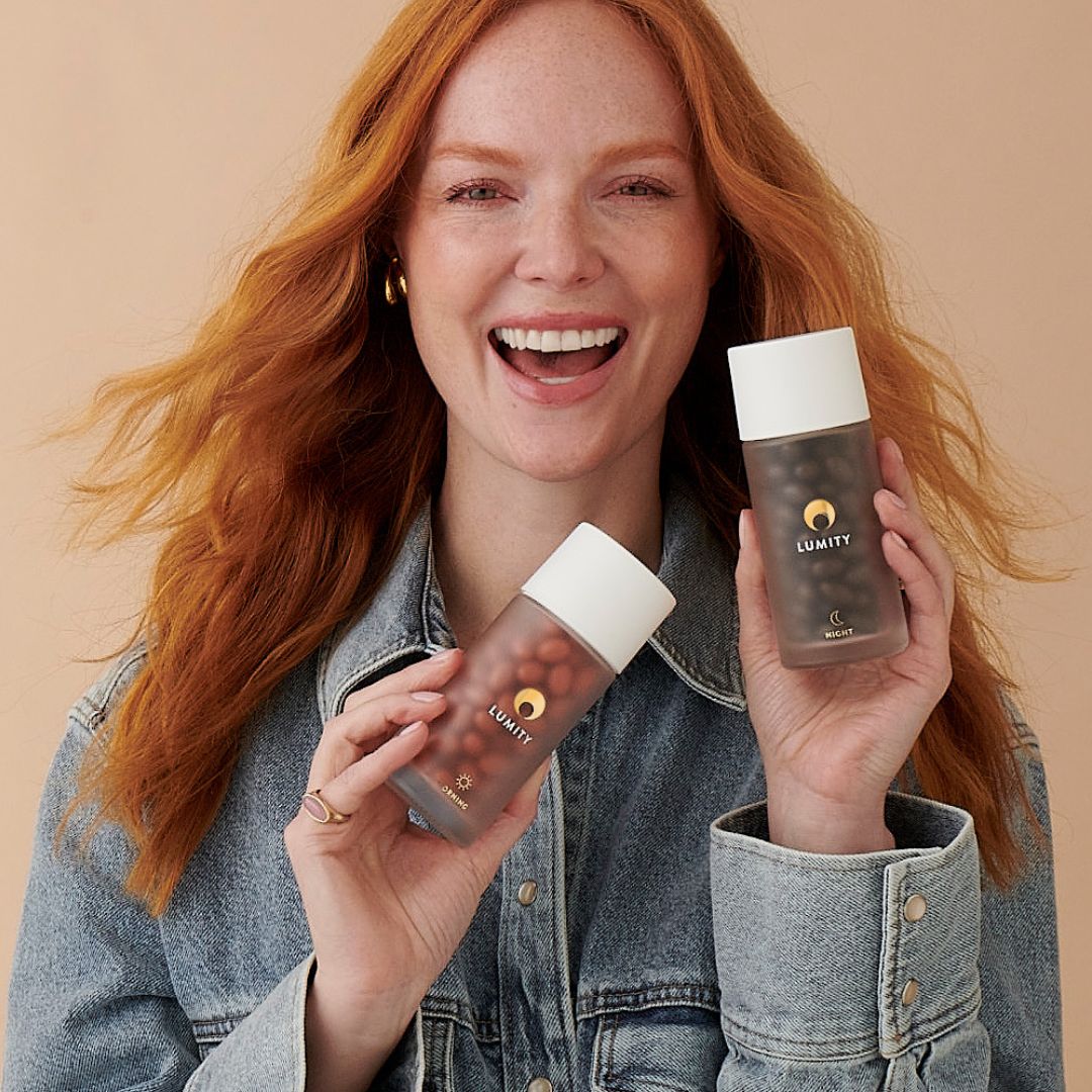 Young woman smiling, holding two frosted Lumity bottles labeled Morning and Night with white caps and small spheres