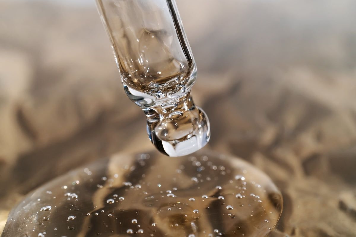 Extreme close-up angled view of a glass dropper dispensing clear gel with small bubbles