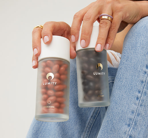Lumity Morning and Night frosted-glass bottles held in hands, white caps, red morning and dark night capsules