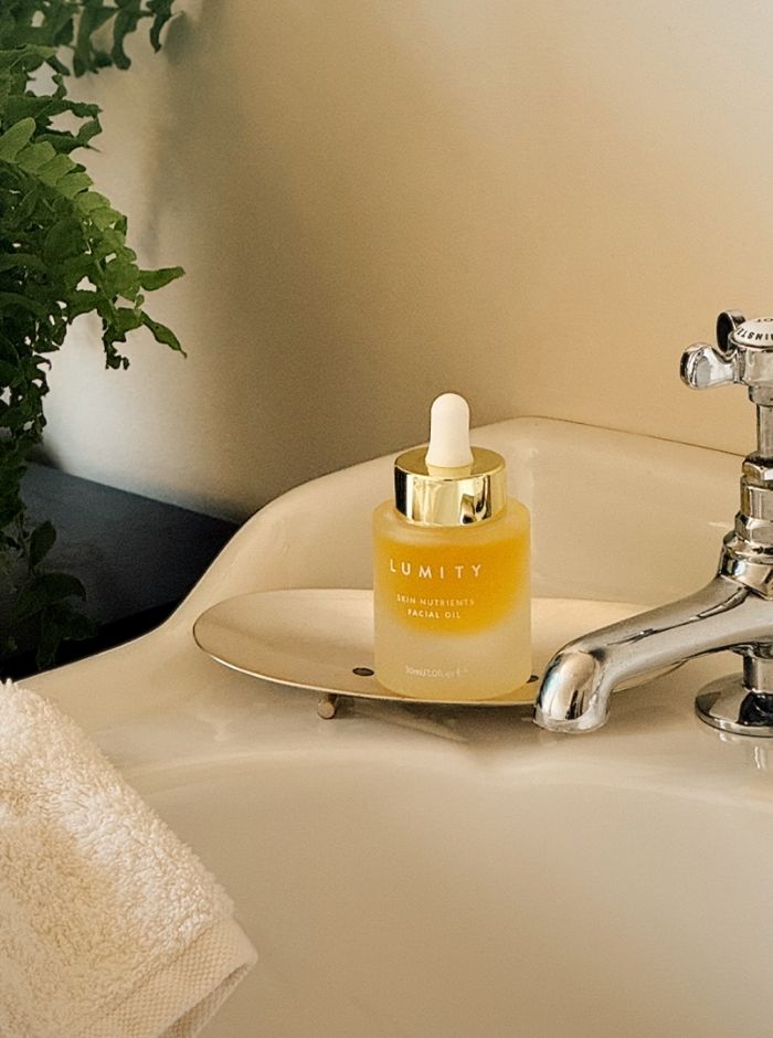 Lumity facial oil bottle on a bathroom counter with a plant and towel in the background.