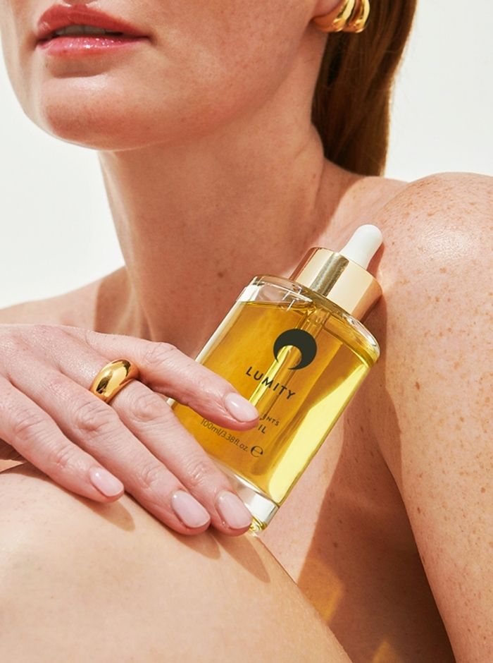 feamle model holding the lumity body oil against her bare skin, wearing gold jewellery