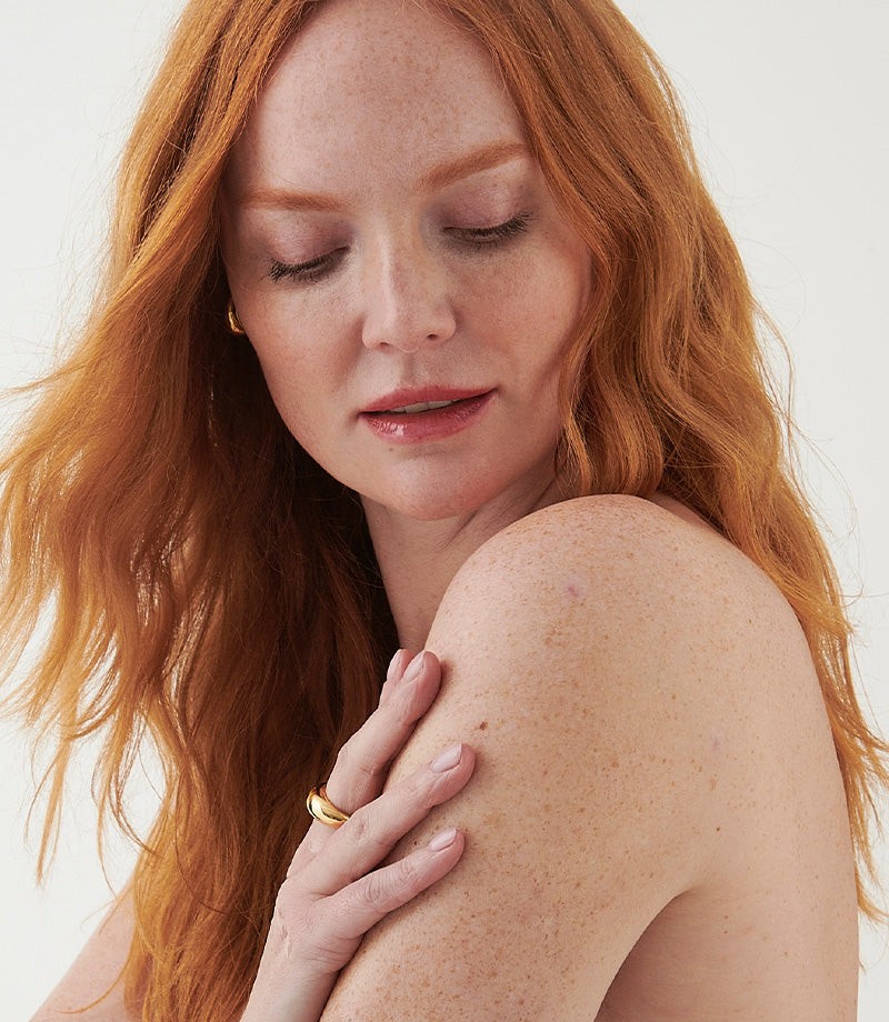 Woman with red hair with hand on her shoulder against a white background