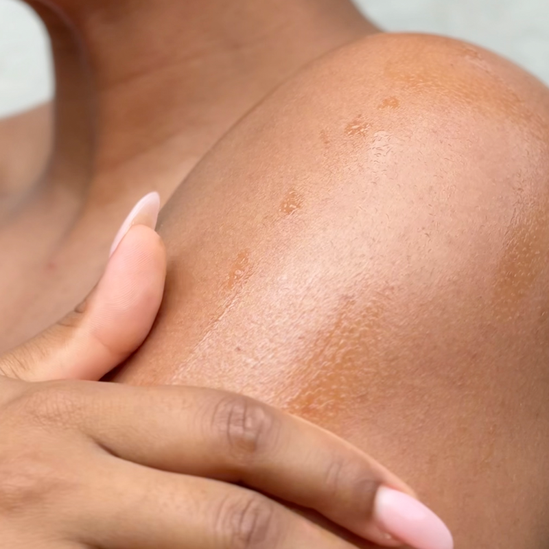 Close-up of a person's shoulder with a hand, showing oil on skin texture.