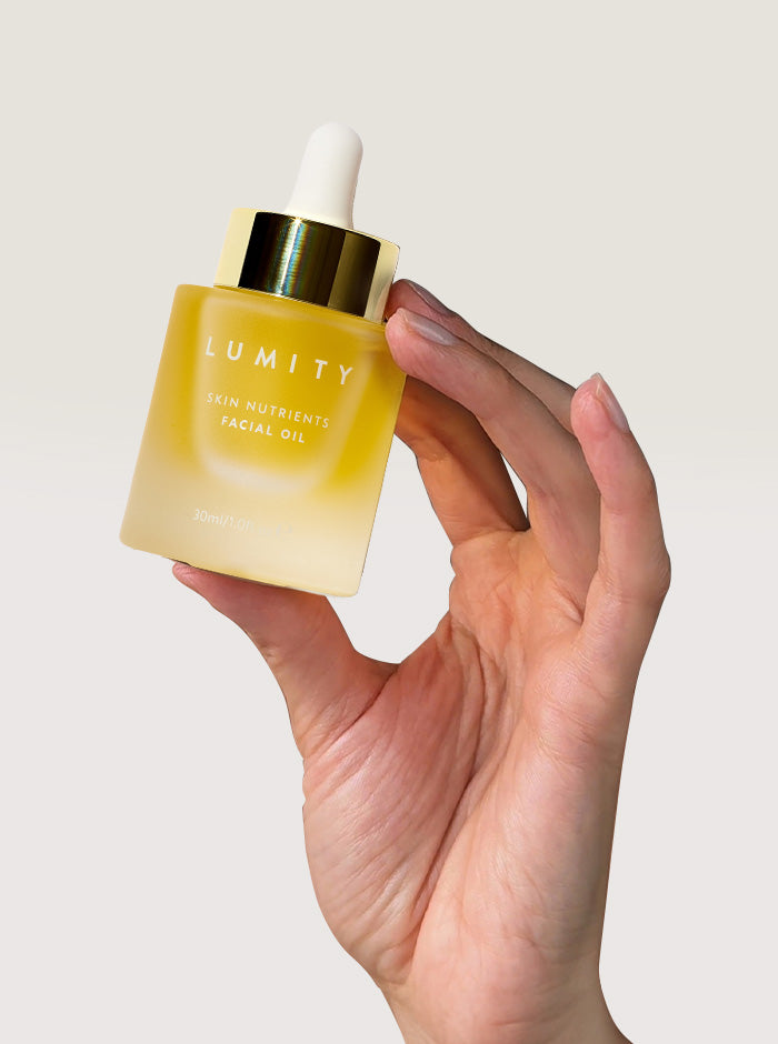 Hand holding a bottle of 'Lumity' facial oil against a plain background