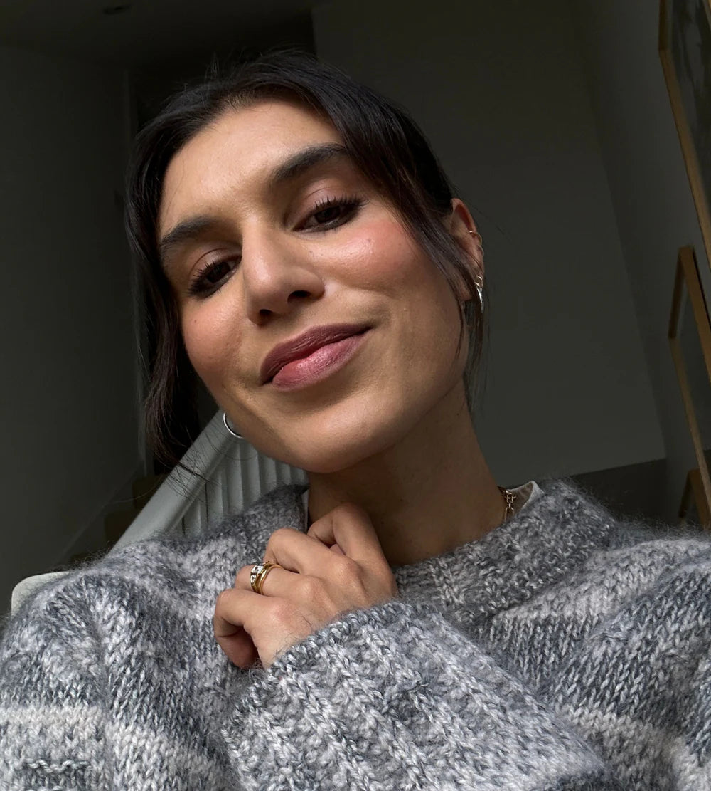 Selfie of a woman wearing a grey sweater, silver jewellery on a blurred background