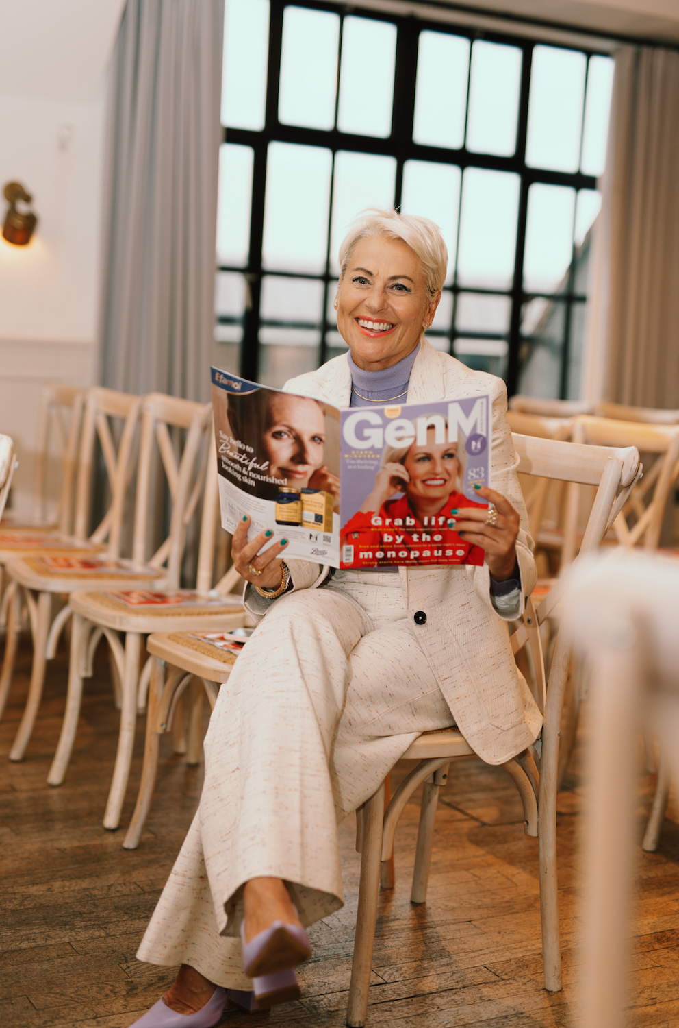Heather Jackson reading GenM  in a room with chairs and large windows.

