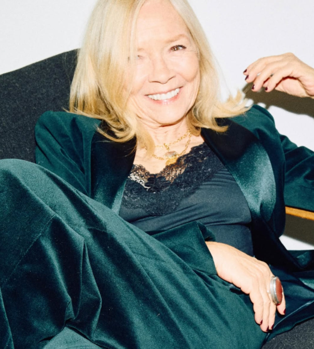 Jo Good wearing a dark green velvet suit and black lace top seated comfortably