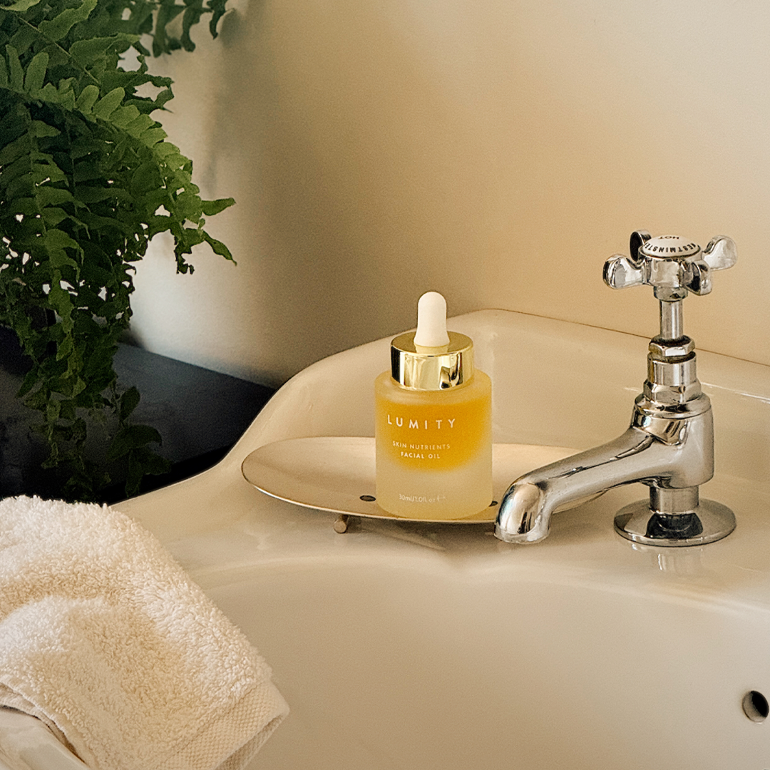 Lumity Facial Oil  bottle on a bathroom sink with a plant in the background