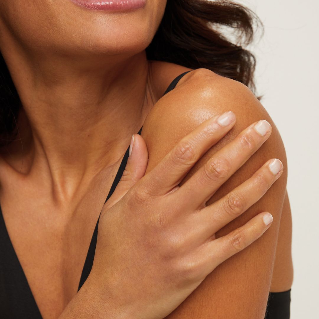 Woman smiling with a hand on her shoulder on a white background