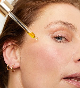 Woman using picker to drop facial oil on face 