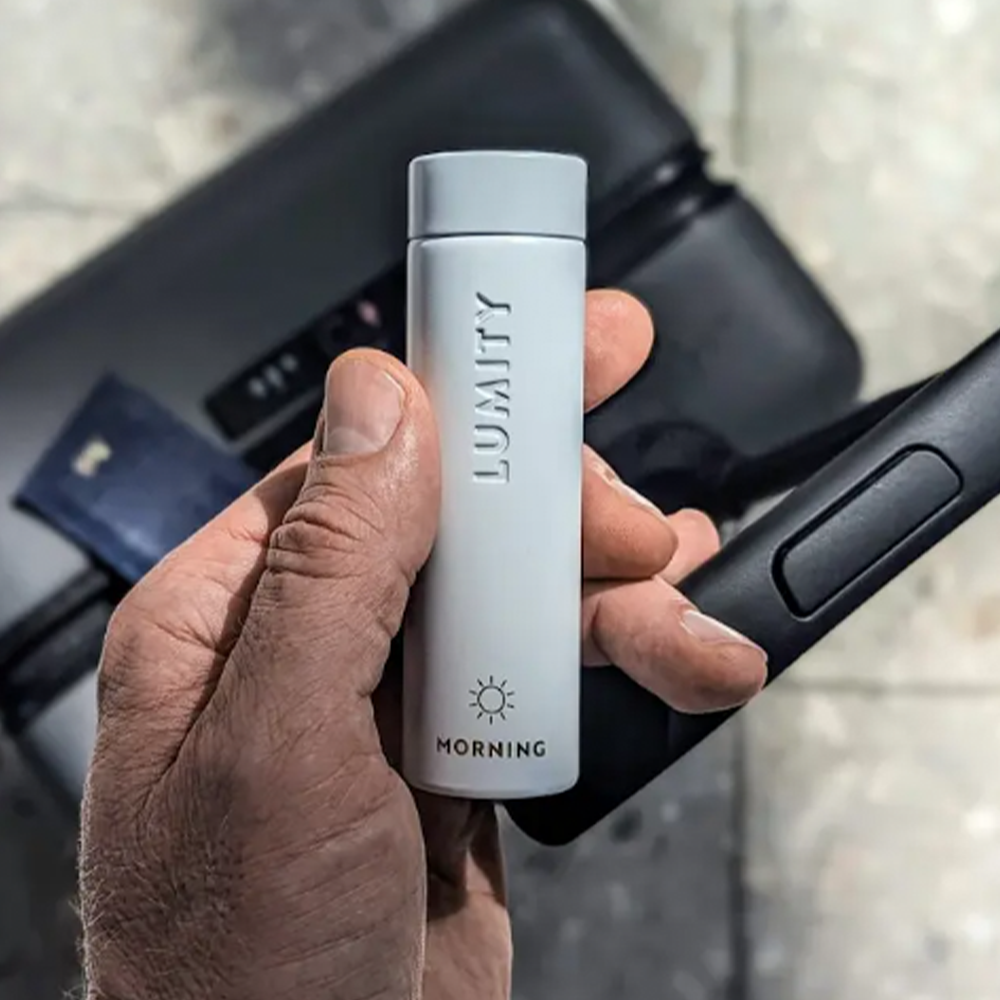 Lumity Morning Travel Case held by a hand with a suitcase and a passport case in the background
