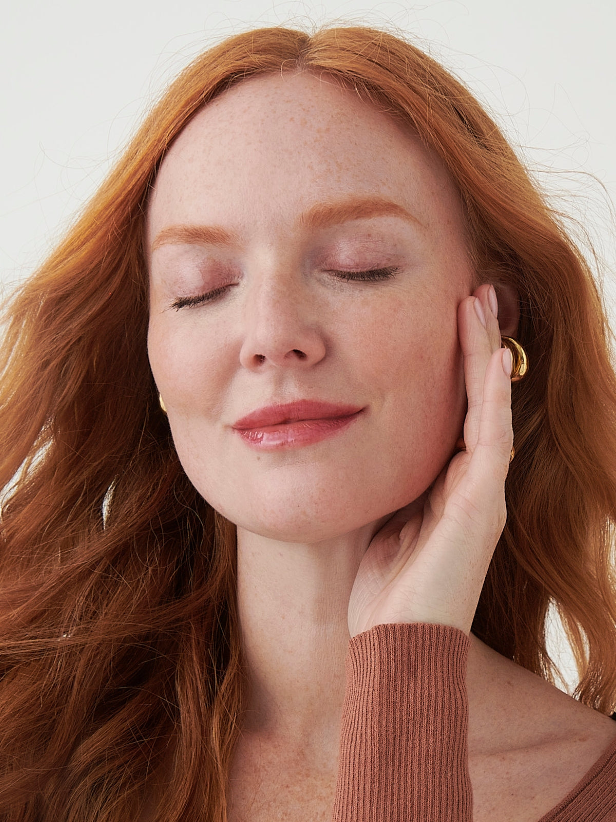 Woman with red hair touching her face against a white background